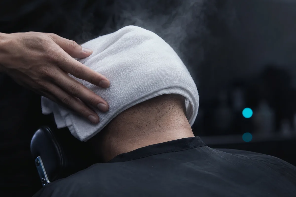 Das heiße Handtuch im Nacken, bevor die Rasur beginnt